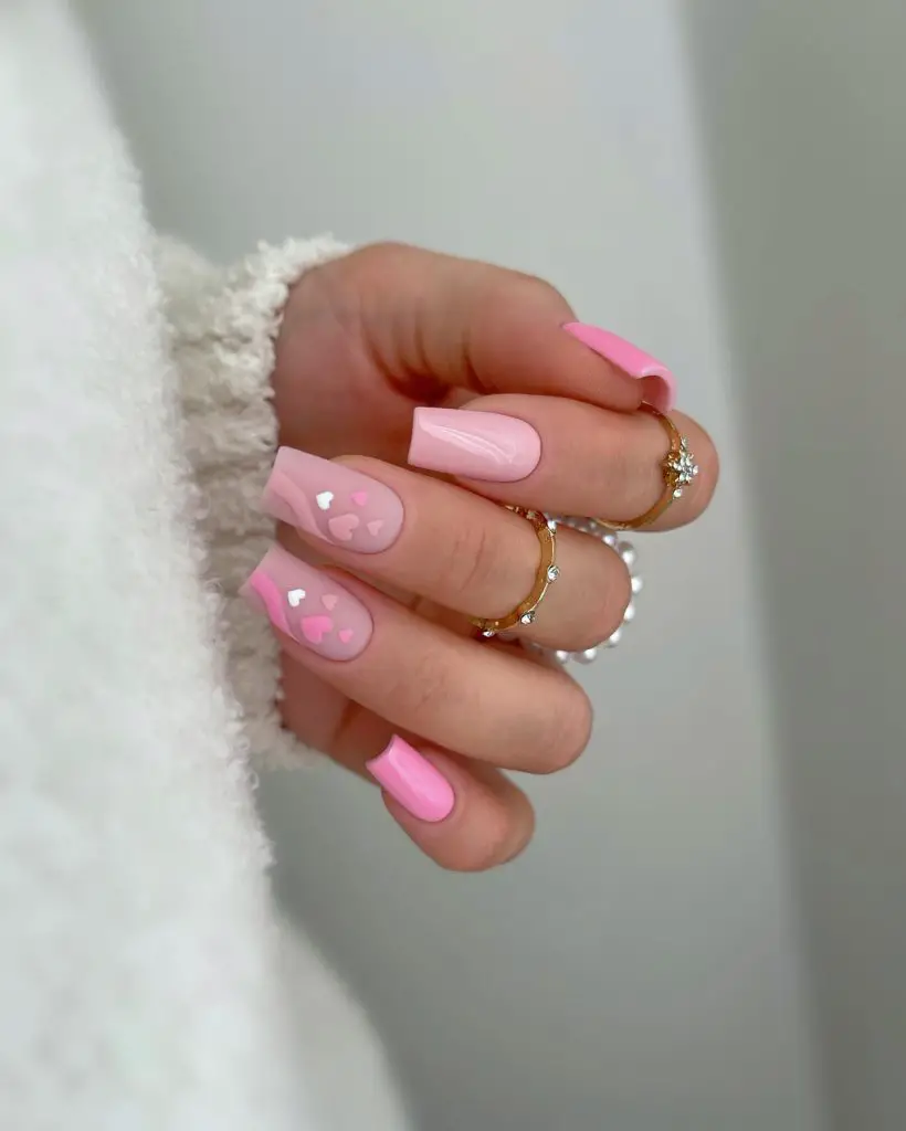 Soft pink matte nails with a mix of solid and negative-space heart designs on a cozy white sweater background